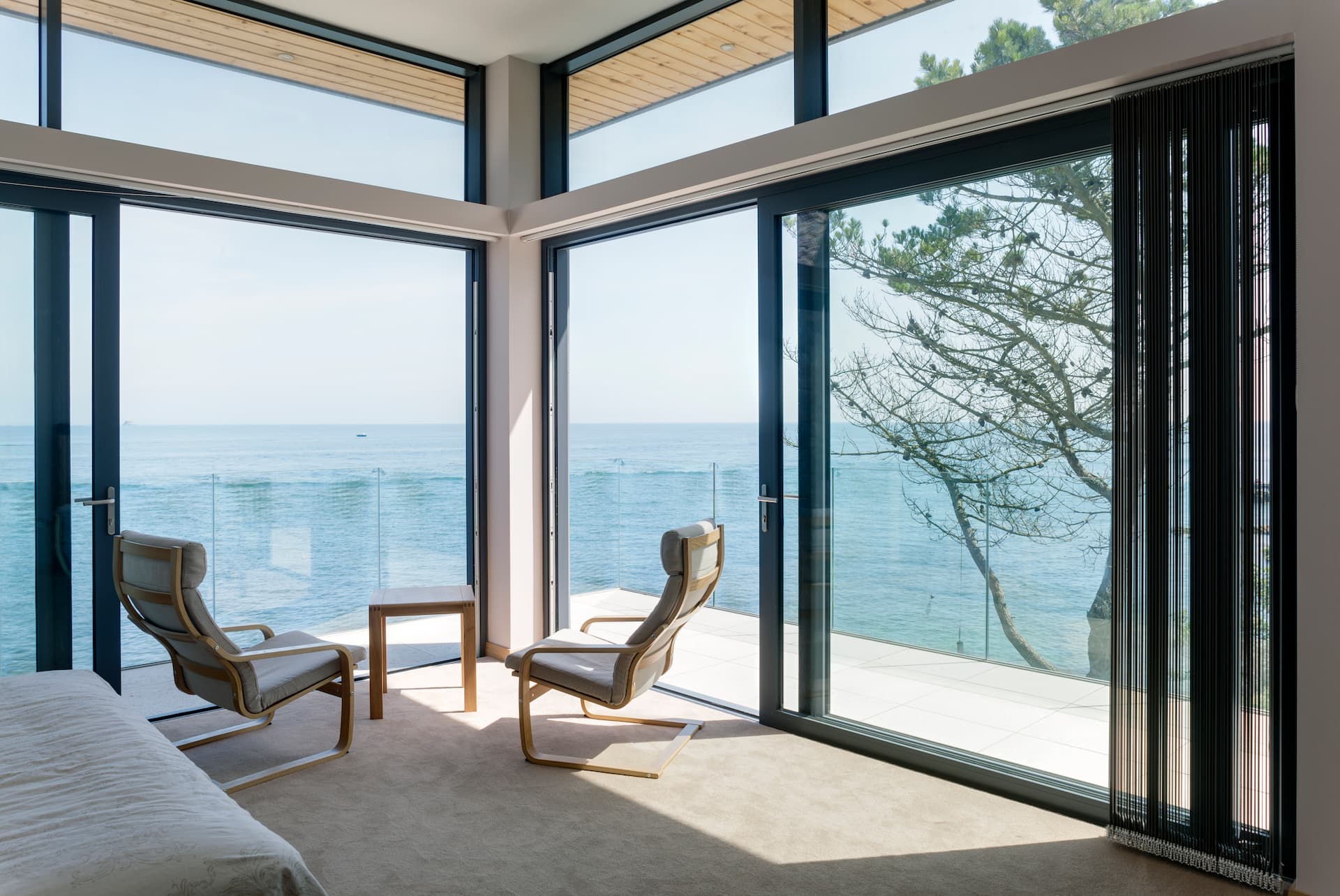 Corner view of the ocean from a modern bedroom, with sliding aluminium patio doors open