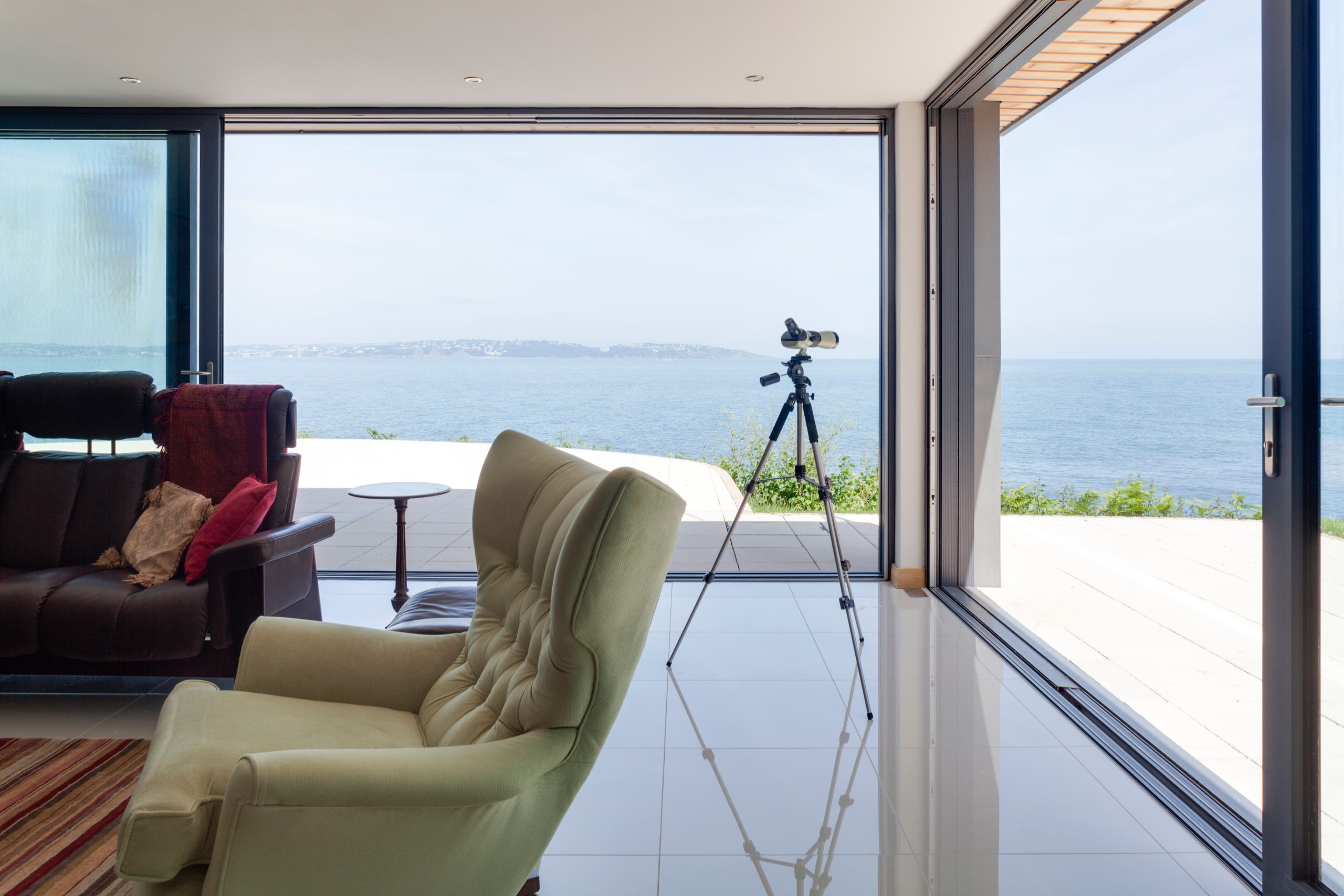 View of the Ocean from a modern living room, with large aluminium patio doors open to enjoy the view